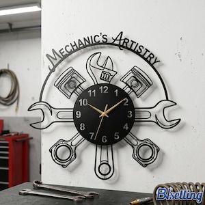 May include: Black metal wall clock with a mechanic theme. The clock features a black clock face with gold hands, surrounded by wrenches, pistons, and the text "Mechanic's Artistry".