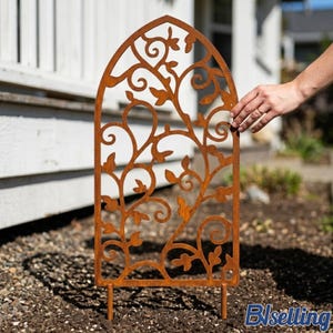 May include: A decorative, arched garden trellis made of rusty brown metal. The trellis features a cut-out design of swirling vines and leaves. Two stakes at the bottom allow for easy placement in the garden. The trellis is shown outdoors in a garden setting.