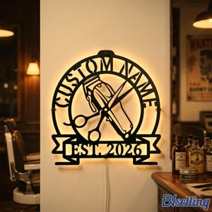 Könnte beinhalten: Ein kreisförmiges Wand-Schild aus schwarzem Metall mit integrierter Hintergrundbeleuchtung, das in der Mitte einen Haarschneider und eine Schere zeigt. Der Text CUSTOM NAME ist oben gebogen und ein Banner unten zeigt EST. 2026.