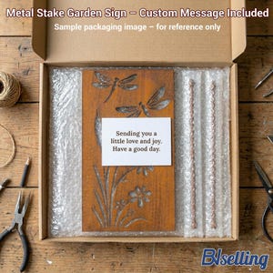 a wooden garden sign with a message, placed in a cardboard box with bubble wrap, and various crafting tools and materials are scattered around the box on a wooden surface.