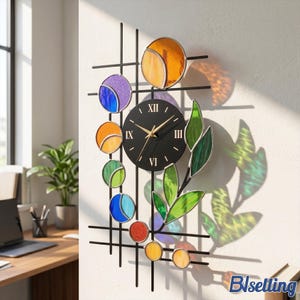 May include: A wall clock featuring a black circular face with gold hands and Roman numerals, mounted on a black metal grid frame. The design includes various circular and leaf-shaped stained glass elements in orange, purple, blue, and green.