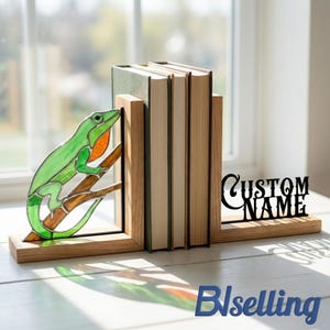 May include: Wooden bookends with a stained glass lizard design. The green and orange lizard is perched on a branch. The bookends hold several books and have a black metal cutout that says "CUSTOM NAME".