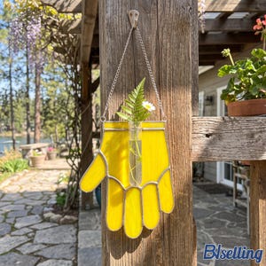 Peut inclure: Une suspension murale en verre teinté jaune en forme de main ouverte avec un tube à essai en verre transparent fixé au centre. L'objet est suspendu par une chaîne en métal argenté et contient une feuille de fougère verte et une petite marguerite.