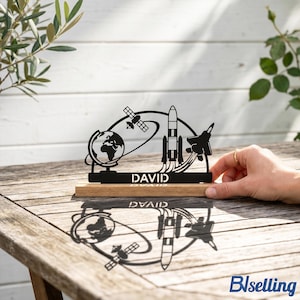 Könnte beinhalten: Schwarze Metall-Schreibtischdekoration zum Thema Weltraum mit Globus, Satellit, Rakete und Düsenjet. Der Name "DAVID" ist auf dem Holzsockel zu sehen. Die Dekoration steht auf einem Holztisch.