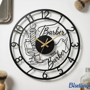 Puede incluir: Reloj de pared de barbería de metal negro con manecillas doradas. El reloj presenta un diseño de poste de barbero, silla y tijeras. Las palabras "Barber" y "The Barber" están escritas en la esfera.