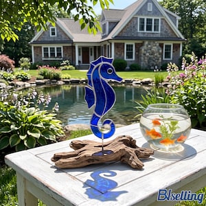 May include: A cobalt blue stained glass seahorse sculpture with a dark eye, mounted on a natural driftwood base. Beside the seahorse sits a clear glass fishbowl containing water, a green aquatic plant, and several small orange goldfish.