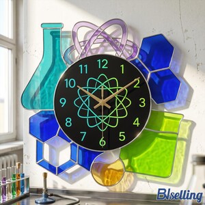 Könnte beinhalten: Eine Wanduhr mit schwarzem, rundem Zifferblatt, grünen Zahlen und einer zentralen Atomgrafik. Die Uhr ist von bunten, durchscheinenden geometrischen Formen umgeben, die an Laborgeräte und chemische Strukturen in Blau, Grün und Gelb erinnern.