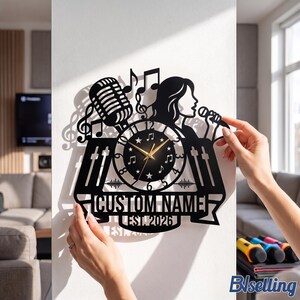 May include: A black wall clock featuring a silhouette of a singer with a microphone, musical notes, and sound mixing sliders. The clock face has gold hands, numbers, and star accents. A banner at the bottom displays the text CUSTOM NAME EST. 2026.