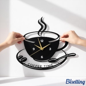 Puede incluir: Reloj de pared negro con forma de taza de café con manecillas doradas y el texto "COFFEE TIME". El reloj incluye un platillo, una cuchara y detalles de granos de café. El reloj está siendo sostenido por dos manos.