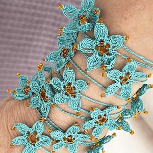 May include: A turquoise crocheted bracelet with gold beads and flower accents.
