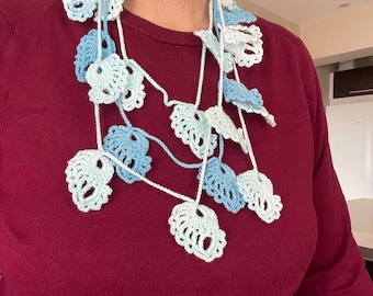 May include: A crocheted necklace with blue and white crocheted flowers. The necklace is layered and has a cascading effect.