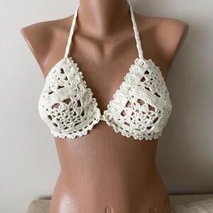 May include: White crochet bikini top with a delicate floral pattern. The top has a halter style with adjustable straps.