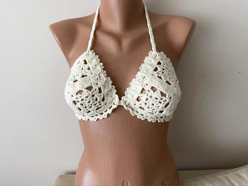 May include: White crochet bikini top with a delicate floral pattern. The top has a halter style with adjustable straps.