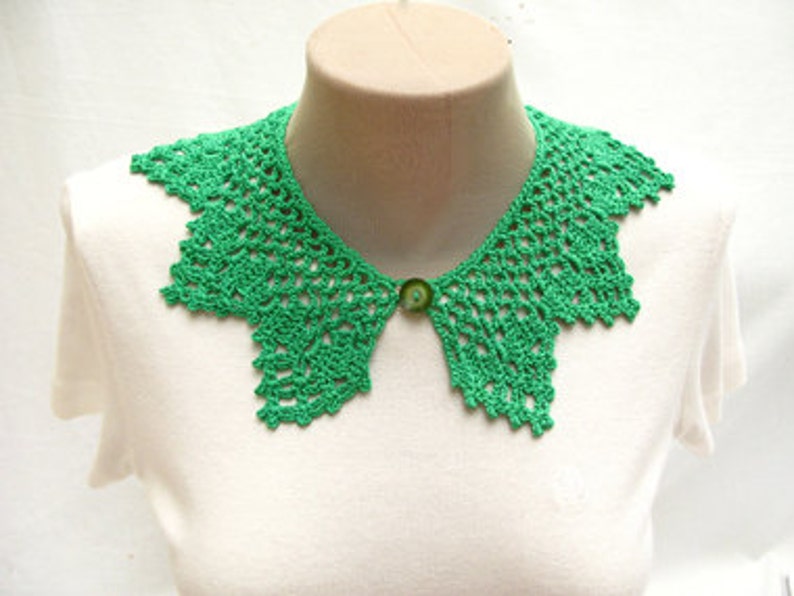 May include: A green crocheted collar with a button closure. The collar is made of delicate lace and has a scalloped edge.