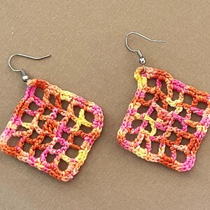May include: A pair of crocheted earrings with a square shape. The earrings are made with a multi-colored yarn in shades of orange, pink, and yellow.