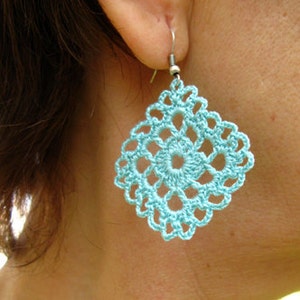 May include: A pair of turquoise blue crocheted earrings with a square shape and intricate design.