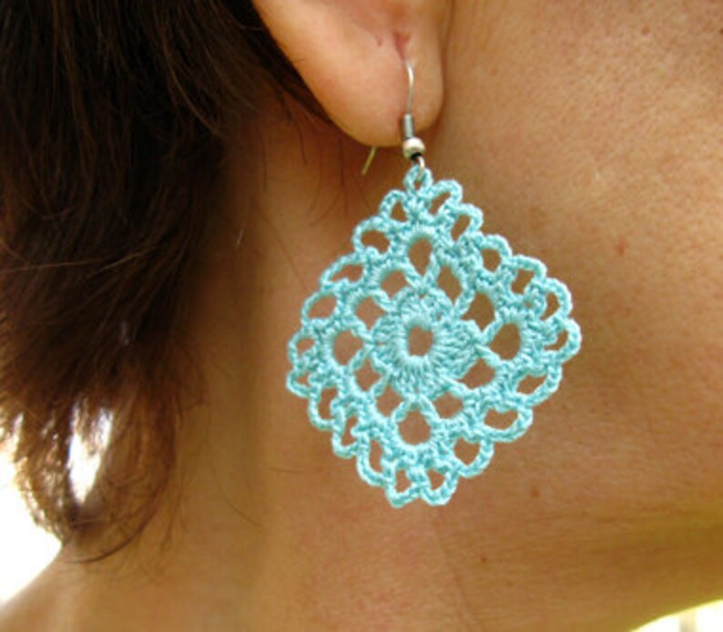 May include: A pair of turquoise blue crocheted earrings with a square shape and intricate design.