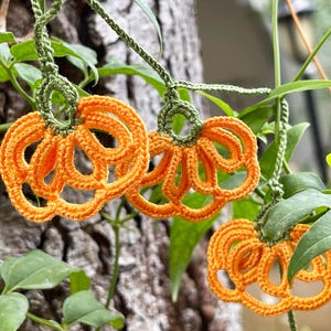 May include: A string of crocheted orange pumpkins with green stems hanging from a vine. The pumpkins are made of yarn and have a delicate, lacy design.