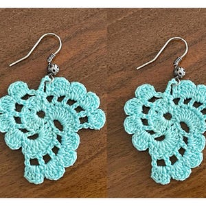 May include: A pair of turquoise crochet leaf earrings. Each earring features a detailed, openwork leaf design with a silver-tone hook. The earrings are displayed on a wooden surface, showcasing the handmade craftsmanship.