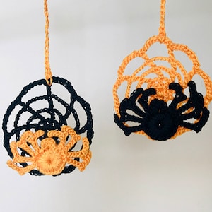 May include: Two crocheted spider web ornaments with spiders hanging from the center. One web is black with an orange spider, and the other is orange with a black spider.