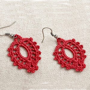 May include: A pair of red crocheted earrings with silver hooks. The earrings are delicate and intricate, with a floral design.
