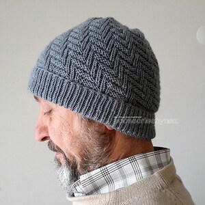 Puede incluir: Un gorro de punto gris con un patr&oacute;n de chevron. El gorro lo lleva puesto una persona con barba.