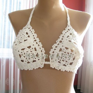 May include: White crochet bikini top with a delicate floral pattern. The top has a halter style with adjustable straps.