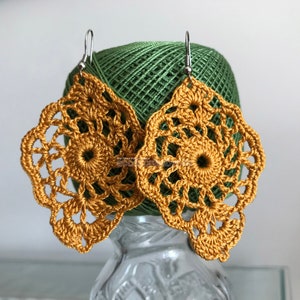 Könnte beinhalten: Ein Paar goldene Häkelohrringe mit einem zarten Blumenmuster. Die Ohrringe hängen an silbernen Haken.