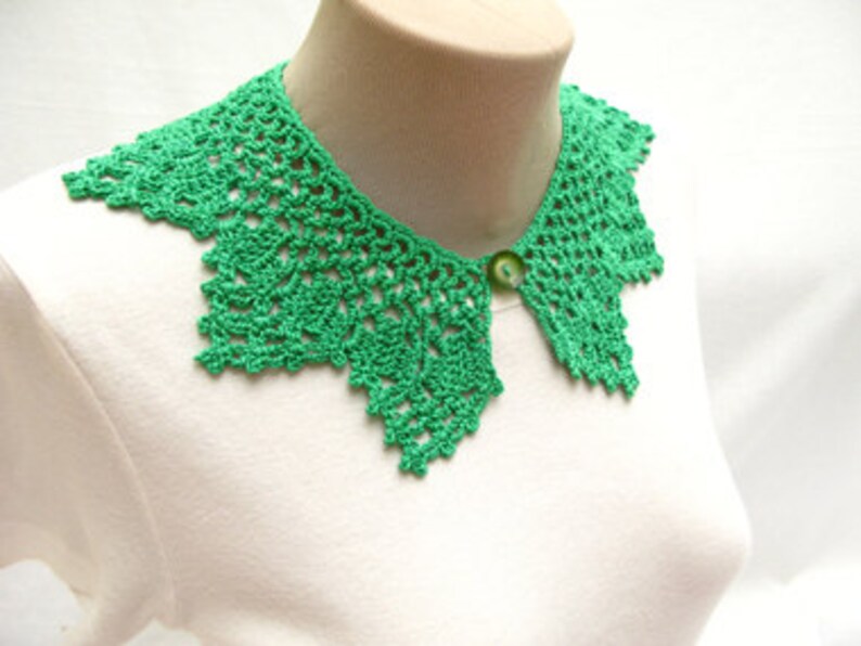 May include: A green crocheted collar with a button closure. The collar is made of delicate lace and has a scalloped edge.