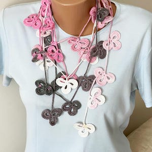 May include: A long crocheted necklace with pink, white, and gray butterfly-shaped charms.