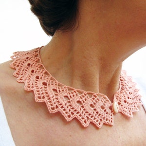 May include: A delicate peach-colored crocheted collar with a single white button closure.
