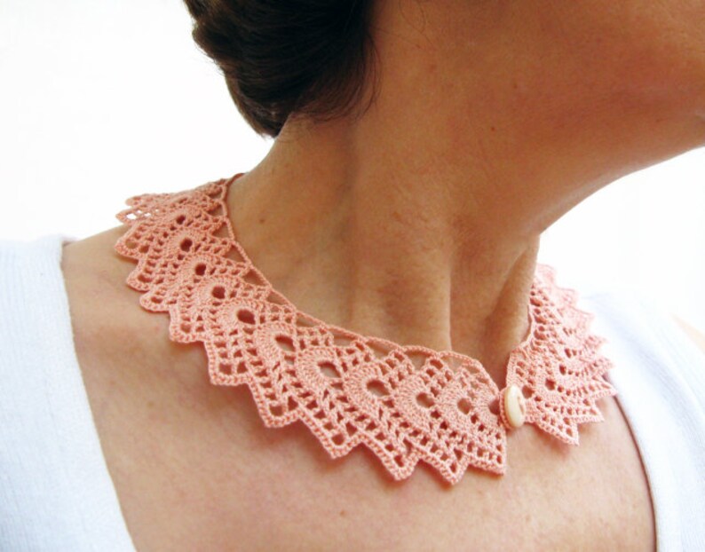 May include: A delicate peach-colored crocheted collar with a single white button closure.