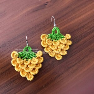 May include: A pair of crocheted earrings shaped like bunches of grapes. The earrings are yellow and green and have silver hooks.