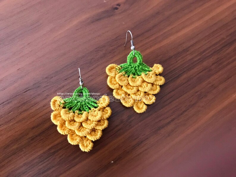 May include: A pair of crocheted earrings shaped like bunches of grapes. The earrings are yellow and green and have silver hooks.