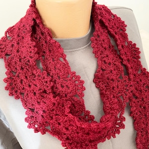 May include: A red crocheted scarf with a delicate floral pattern. The scarf is made of soft yarn and is perfect for adding a touch of elegance to any outfit.