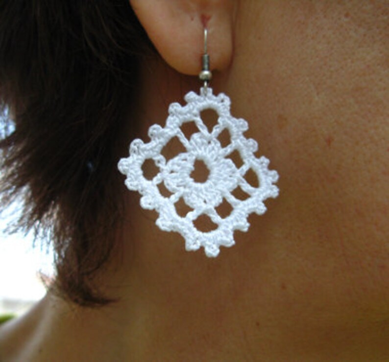 May include: White crocheted earrings with a square design. The earrings are attached to silver hooks.