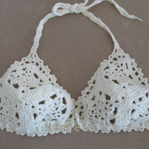 May include: White crocheted bikini top with a delicate floral pattern. The top has adjustable straps and a halter neck style.