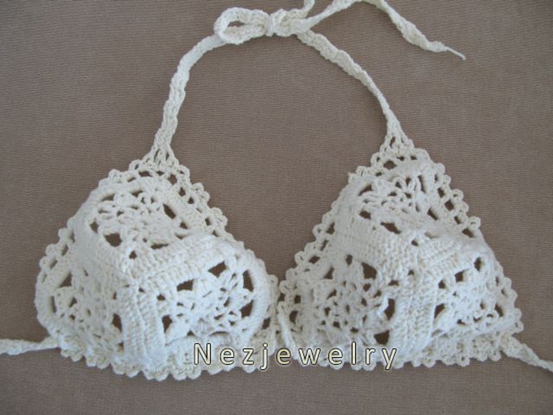 May include: White crocheted bikini top with a delicate floral pattern. The top has adjustable straps and a halter neck style.