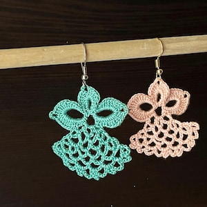 May include: A pair of crocheted earrings, one is teal and the other is pink. The earrings are hanging from a wooden dowel.