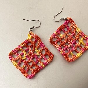 May include: A pair of crocheted earrings with a geometric design in shades of orange, pink, and yellow.