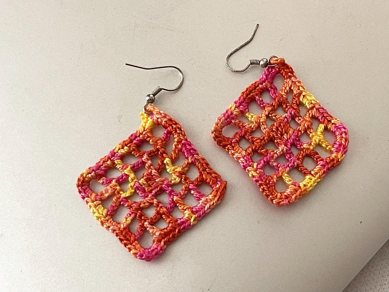 May include: A pair of crocheted earrings with a geometric design in shades of orange, pink, and yellow.
