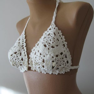May include: White crocheted bikini top with a halter style and a delicate floral pattern. The top is shown on a white mannequin.