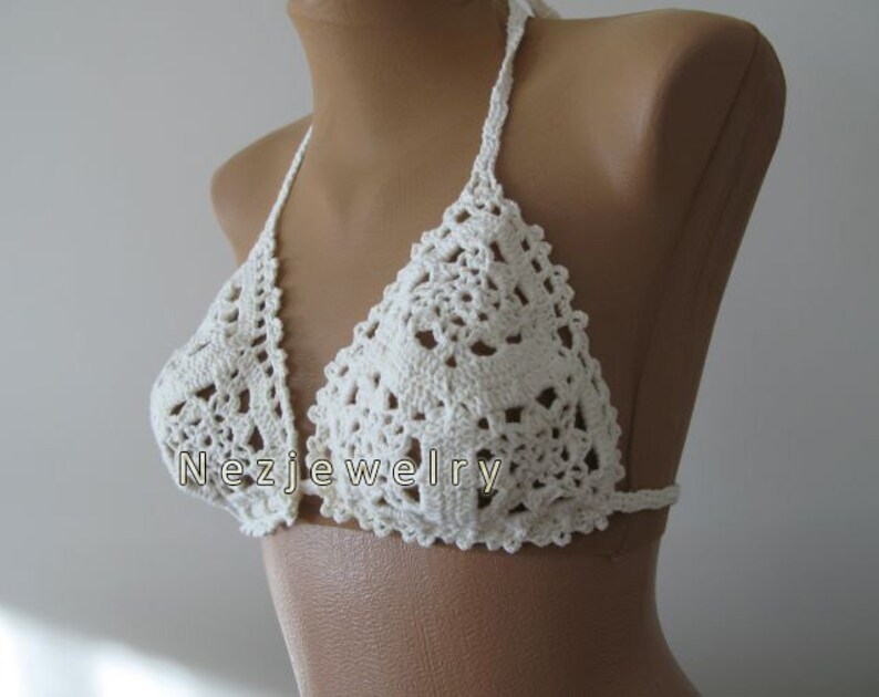 May include: White crocheted bikini top with a halter style and a delicate floral pattern. The top is shown on a white mannequin.