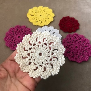 May include: Five crocheted doilies in various colors, including white, yellow, pink, and red. The doilies are all circular and have a delicate, lacy design.