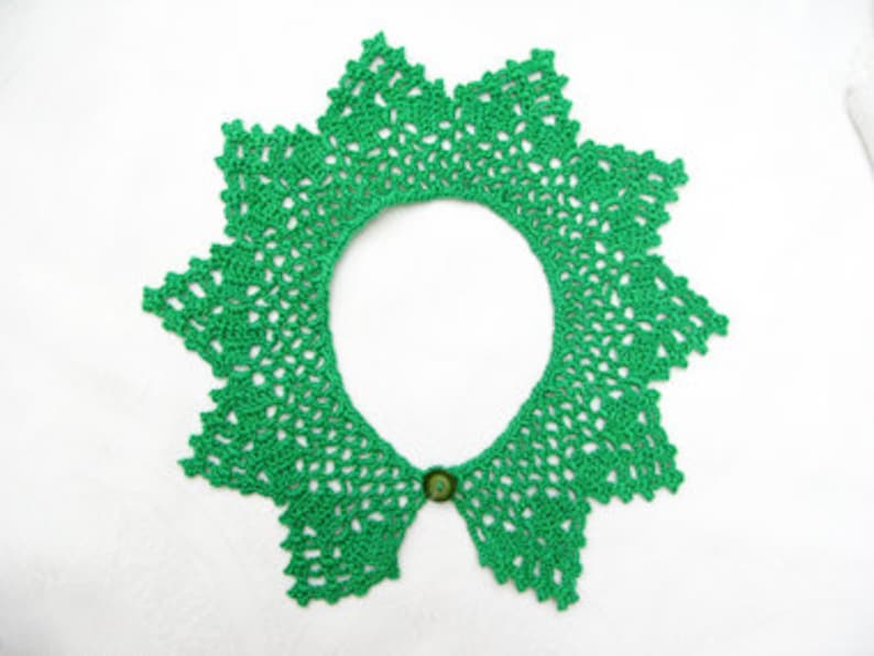 May include: A green crocheted collar with a button closure. The collar is made with a delicate lace pattern.