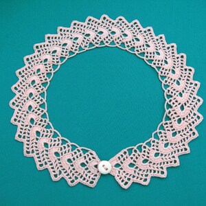 May include: A delicate pink crocheted collar with a white button closure. The collar is made of intricate lacework and has a scalloped edge.