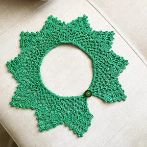 May include: A green crocheted collar with a button closure. The collar is made of delicate lace and has a scalloped edge.