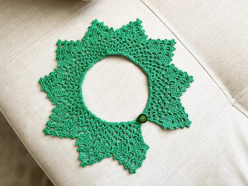 May include: A green crocheted collar with a button closure. The collar is made of delicate lace and has a scalloped edge.