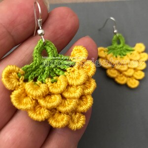 May include: Crocheted grape earrings with yellow and green yarn. The earrings are hanging from silver hooks.
