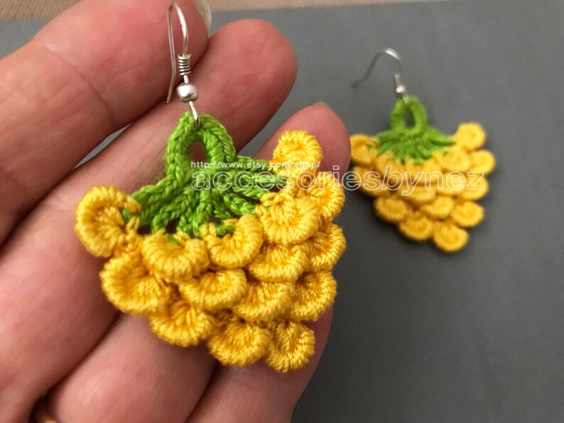 May include: Crocheted grape earrings with yellow and green yarn. The earrings are hanging from silver hooks.